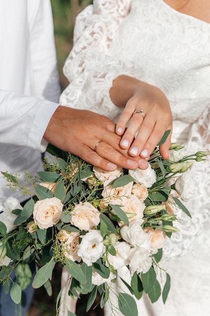 Mani della sposa e dello sposo con anelli sul bouquet da sposa Concetto di matrimonio