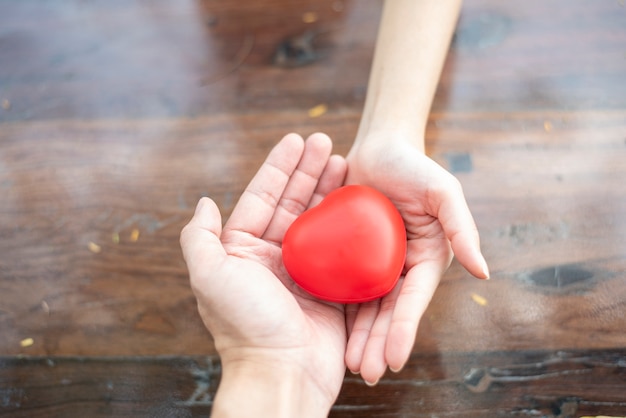 Mani delle coppie che tengono cuore rosso