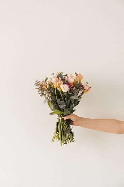 Mani delle donne che tengono bouquet di fiori contro il muro bianco