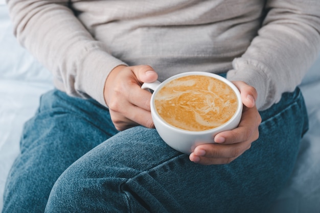 Mani delle donne che tengono tazza di caffè latte