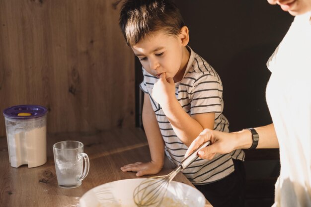 Mani delle madri che mescolano gli ingredienti per l'impasto con il figlio in cucina moderna, il genitore che aiuta il bambino, la famiglia, noi...