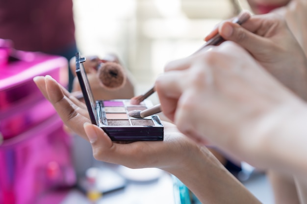 Mani delle ragazze del gruppo che tengono la spazzola e la tavolozza di trucco per trucco, concetto di bellezza