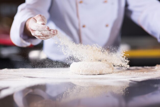 mani dello chef che preparano l'impasto per la pizza sul tavolo cosparso di farina di primo piano