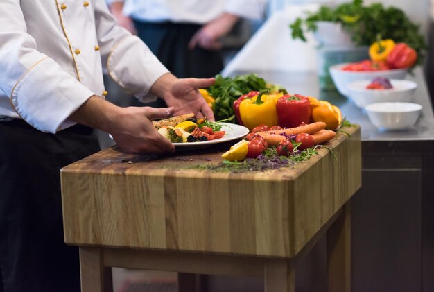 Mani dello chef che tengono filetto di pesce salmone fritto con verdure per cena nella cucina di un ristorante