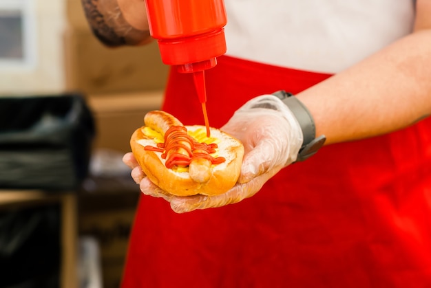 Mani dello chef di strada che aggiungono ketchup su hot dog da vicino