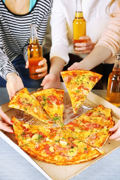 Mani di amici con bottiglie di birra e pizza, primi piani