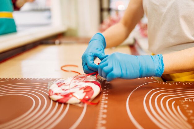 Mani di artigiano in guanti avvolge lecca-lecca cotto fresco. Produzione di caramello in officina. Divertimento in vacanza nel negozio di caramelle