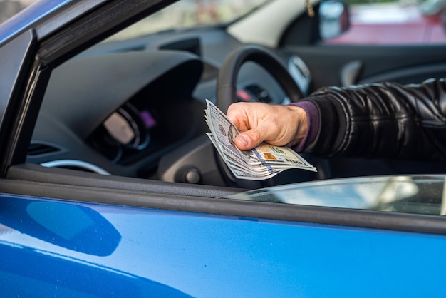 Mani di automobilisti maschi che tengono nuove banconote in dollari al centro negli interni dell'auto Concetto di business