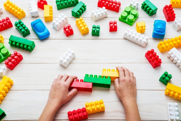 Mani di bambino che giocano con blocchi di plastica colorati sullo sfondo bianco del tavolo di legno