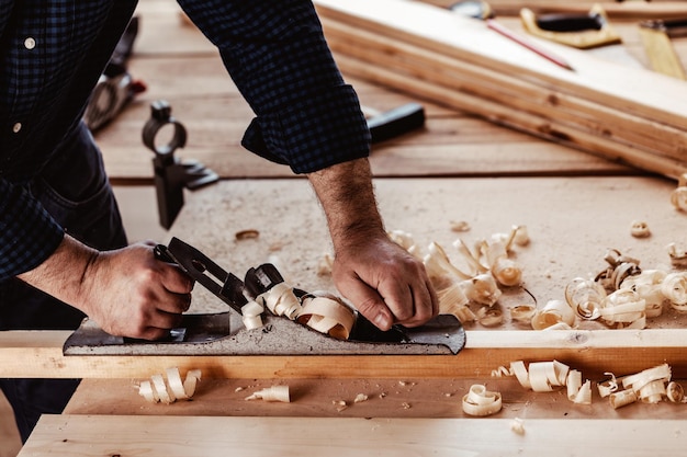 Mani di carpentieri che piallano una tavola di legno con una pialla a mano