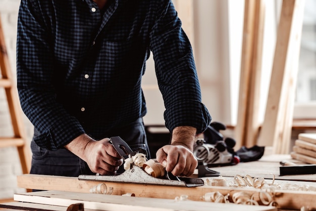 Mani di carpentieri che piallano una tavola di legno con una pialla a mano