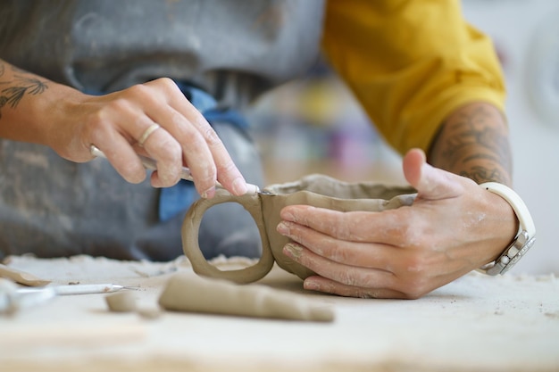 Mani di ceramista che modellano una tazza di ceramica di materiale di argilla grezza utilizzando strumenti di vasaio professionali in officina