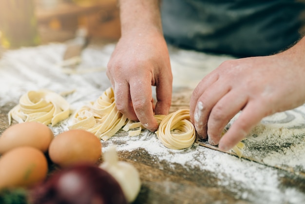 Mani di chef maschio che preparano pasta fresca sul tavolo da cucina in legno. Processo di preparazione delle fettuccine