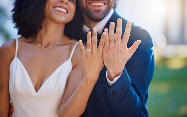 Mani di coppia sposata e fedi nuziali con sorriso per impegno matrimoniale o luna di miele all'aperto Mano di sposo e sposa felici che sorridono e mostrano anello in simbolo per moglie e marito