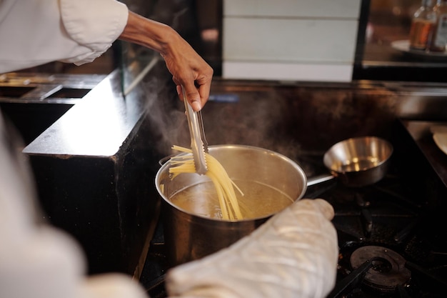 Mani di cuoco che usano le pinzette da cucina quando togliono gli spaghetti dalla padella