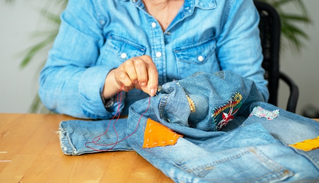 Mani di donna anziana che cuciono su un tessuto jeans