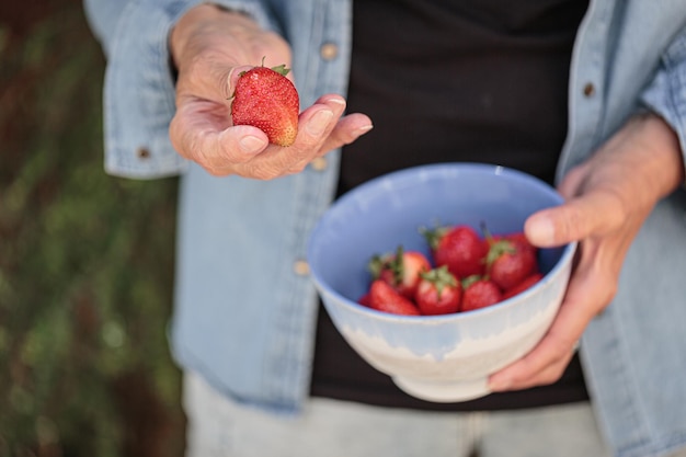 Mani di donna anziana in possesso di una ciotola di fragole mature