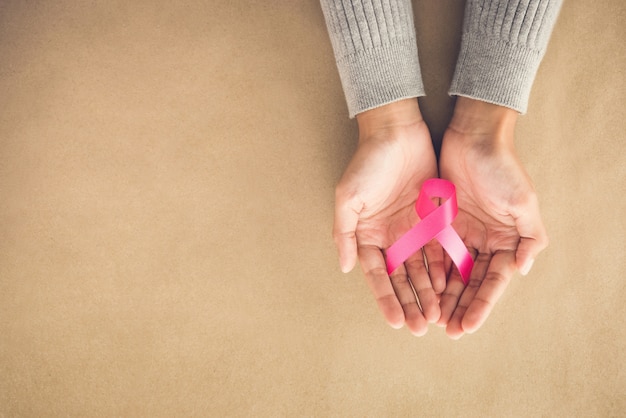 Mani di donna che danno nastro di raso rosa, simbolo di sostegno della campagna di sensibilizzazione sul cancro al seno in ottobre,