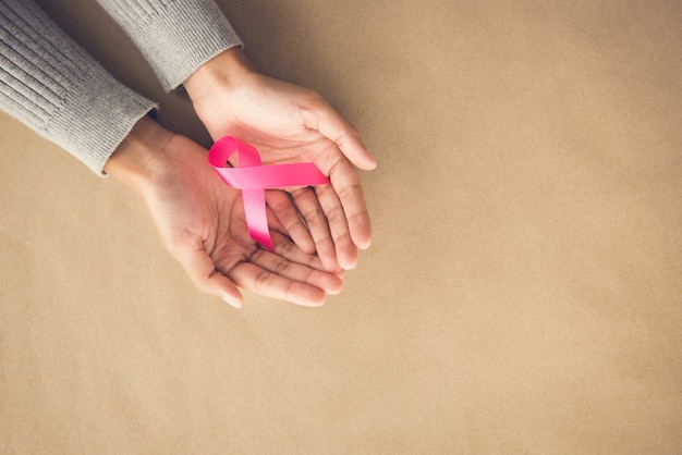 Mani di donna che danno una campagna in nastro rosa satinato ad ottobre,