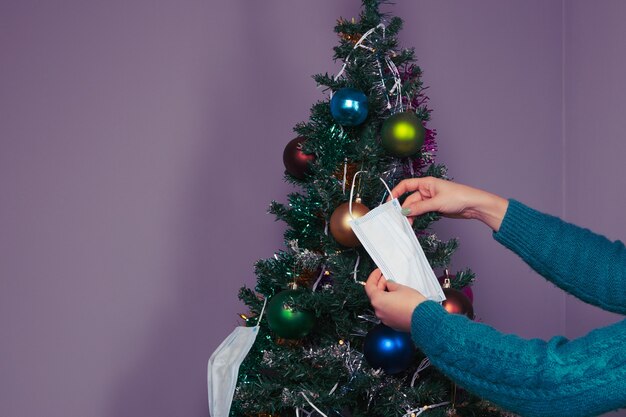 Mani di donna che decorano l'albero di Natale con maschere per il viso come simbolo del coronavirus