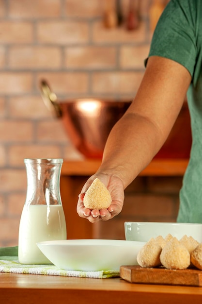 Mani di donna che impanano la crocchetta brasiliana coxinha de frango con pangrattato su un tavolo da cucina in legno