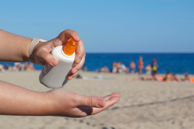 Mani di donna che mettono la crema solare in spiaggia