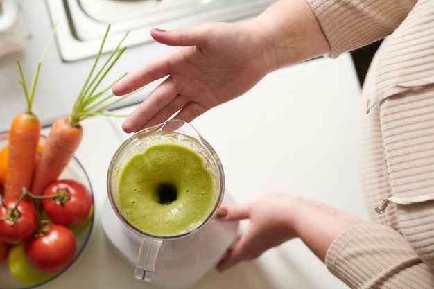 Mani di donna che mostrano frullatore con frullato verde delizioso fresco che ha preparato per colazione