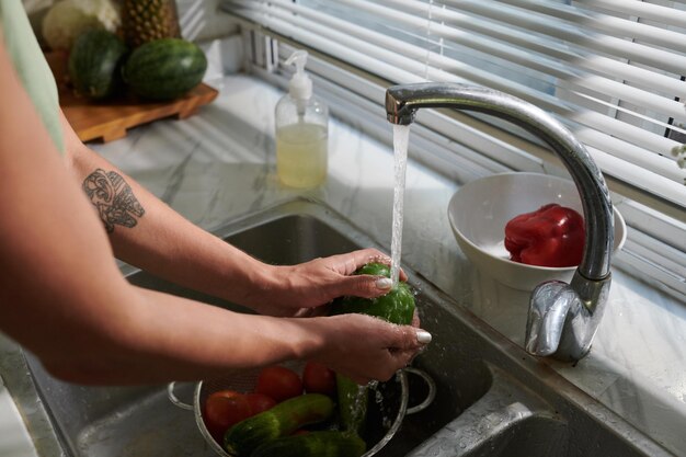Mani di donna che sciacquano le verdure nel lavello della cucina
