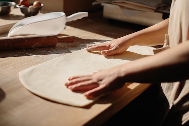 Mani di donna che stendono la pasta nella farina con il mattarello in panetteria