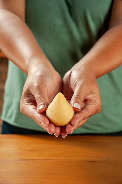 Mani di donna che tengono crocchetta brasiliana coxinha de frango su un tavolo da cucina in legno