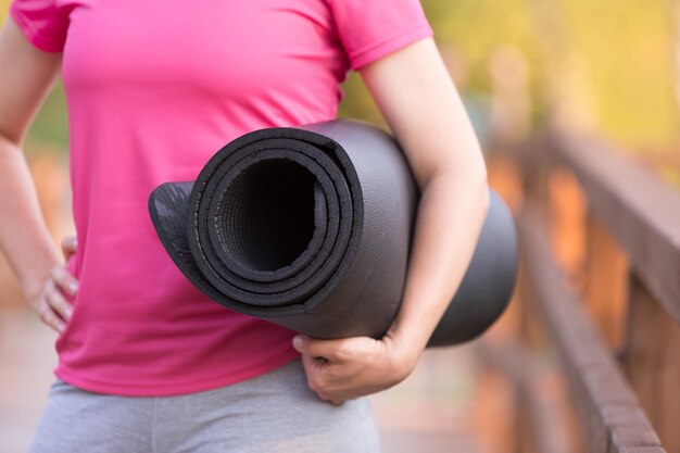 Mani di donna che tengono tappetino da yoga Ragazza che si esercita all'aperto Concetto di fitness e stile di vita sano