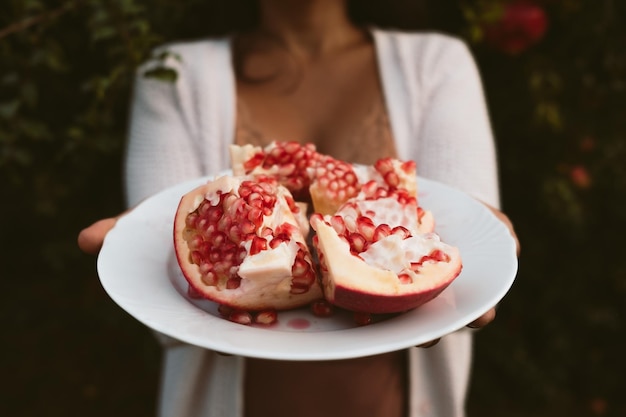 Mani di donna che tengono un piatto con semi rossi di melograno fresco raccolti dall'albero sullo sfondo