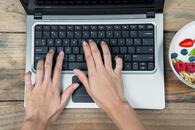 Mani di donna che utilizzano un computer portatile all'ora di colazione