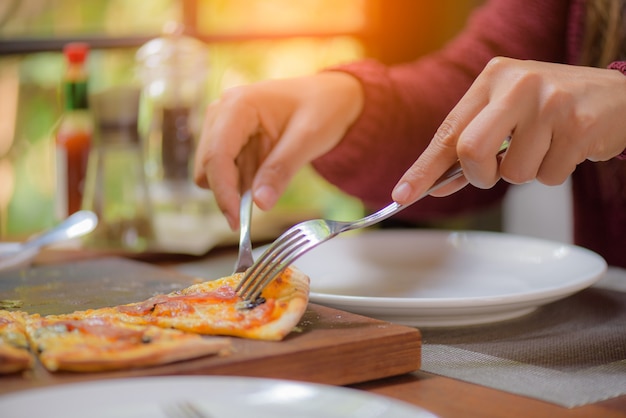 Mani di donna con cucchiaio e forchetta prendendo fette di pizza.