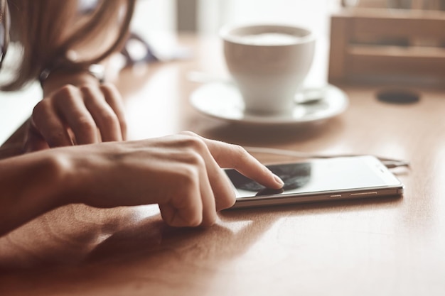 Mani di donna con cuffie per smartphone e tazza di tè per il montaggio del display grafico