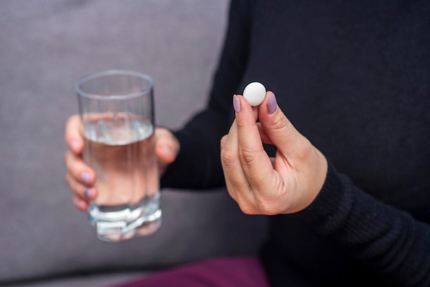 Mani di donna con pillole e un bicchiere d'acqua