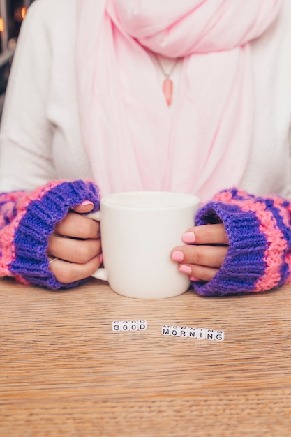 Mani di donna con tazza bianca e blocchi di lettere sul tavolo di legno. Buongiorno concetto.