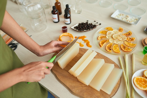 Mani di donna creativa che tagliano la base di sapone quando si fanno le barrette detergenti agli agrumi