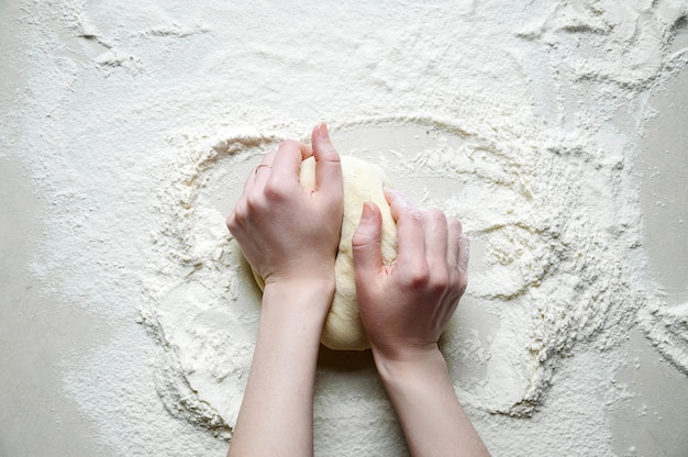 Mani di donna impasta la pasta con farina sul tavolo da cucina bianco. Vista dall'alto.