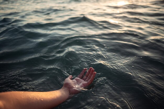 Mani di donna in acqua che ti invitano sopra i raggi dorati del tramonto