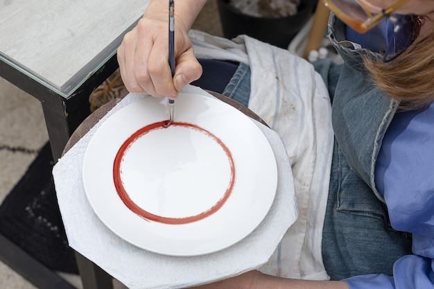 Mani di donna irriconoscibili che lavorano pittura piatti in ceramica. Concetto di artigianato