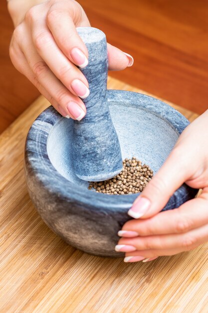 Mani di donna macinare pepe nero da pestello in un mortaio di granito grigio sul tavolo.