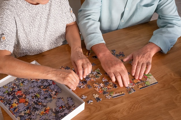 Mani di due anziani a casa che giocano con il puzzle sul tavolo di legno wooden