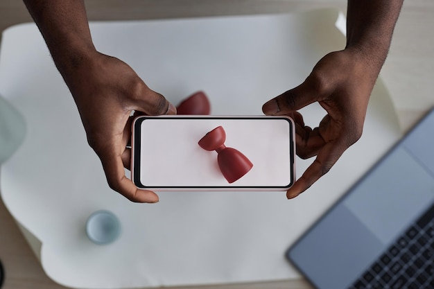 Mani di giovane artigiano con smartphone che scattano foto della tazza rossa