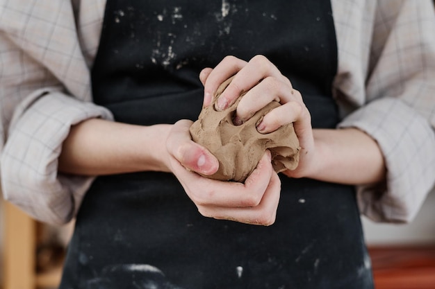 Mani di giovane donna creativa in abiti da lavoro che tengono un pezzo di argilla morbida