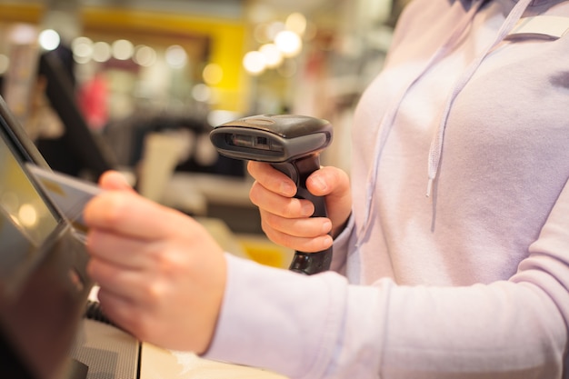 Mani di giovane donna utilizzando scanner per la scansione di merci per un cliente in un enorme centro commerciale