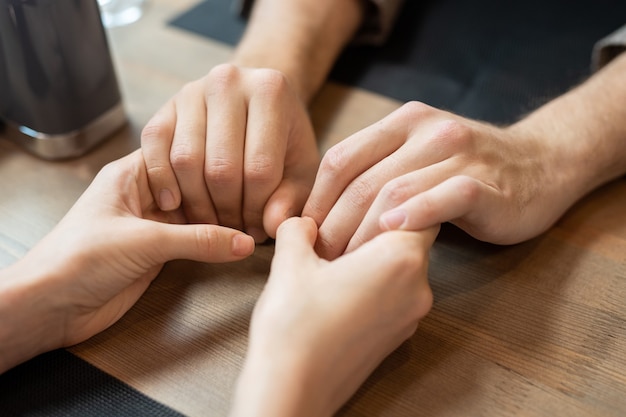 Mani di giovani appuntamenti amorosi e affettuosi seduti al tavolo servito durante una cena romantica in un ristorante o bar contemporaneo