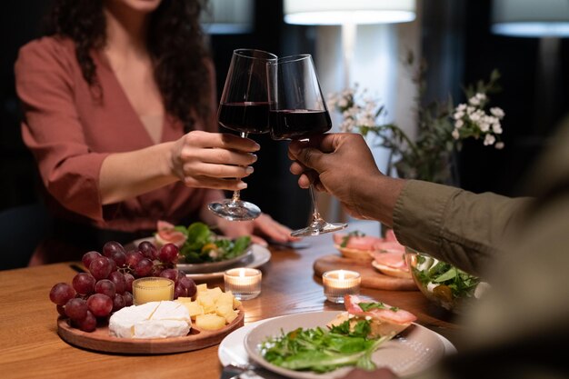 Mani di giovani appuntamenti interrazziali che tintinnano con bicchieri di vino rosso