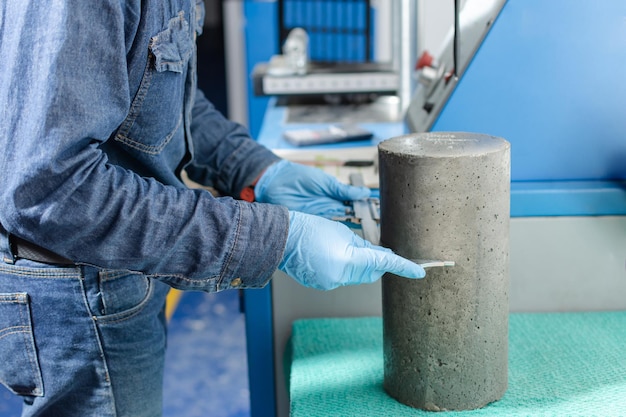 Mani di operaio industriale maschio con guanti in lattice blu che misurano un cilindro di cemento