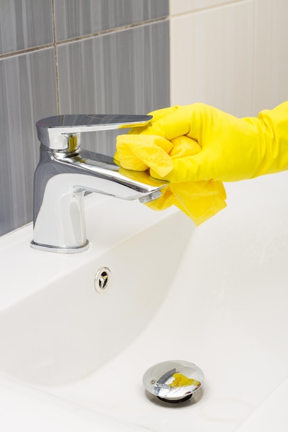 Mani di pulizia primaverile con guanti gialli lavando il rubinetto di metallo del bagno